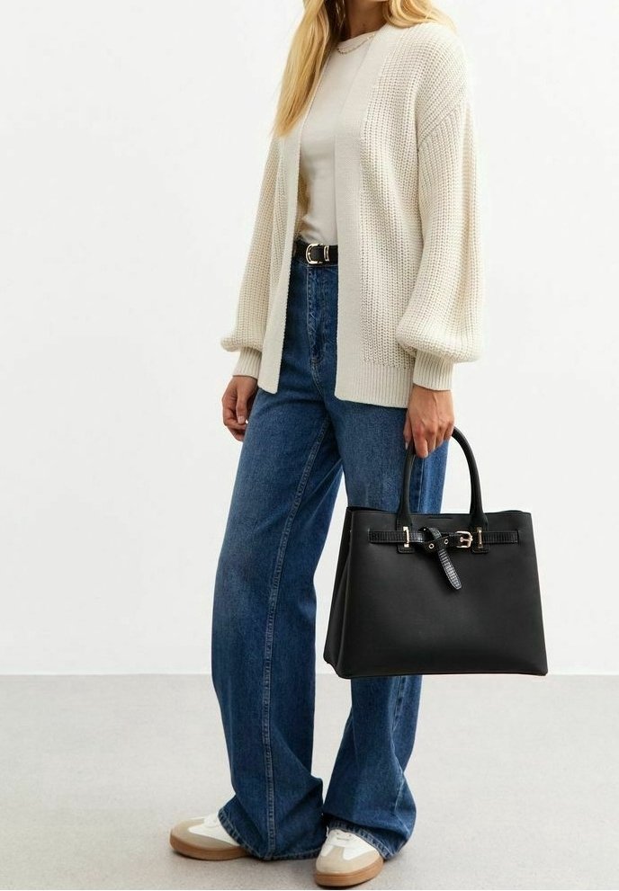 Femme portant un cardigan en maille crème, un t-shirt blanc, un jean bleu à jambes larges, des baskets blanches, tenant un sac à main en cuir noir avec détail boucle.