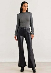 Pantaloni in finta pelle nera a campana con vita alta, abbinati a un top fitted grigio a maniche lunghe a coste, con scollatura rotonda.