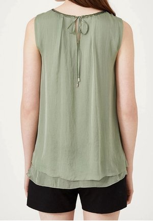 Ärmellose, hellgrüne Bluse mit mehrlagigem Saum und gebundener Schlitzverschluss am hinteren Ausschnitt, kombiniert mit schwarzen Shorts.