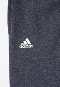 Szare dresy z polaru z białym logo adidas z boku. Miękka tekstura, luźny krój, bez widocznych wzorów ani akcentów.