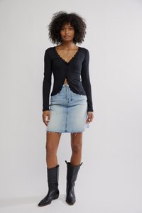 Crna bluza s dugim rukavima s čipkastim rubom, svijetloplava traper suknja, poderani rub i crne kaubojske čizme s šiljatim vrhovima.