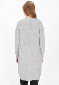 Langer, hellgrauer Strickpullover aus weichem, flauschigem Material mit lockerer Passform und Rippmuster. Rundhalsausschnitt und Seitenschlitze.