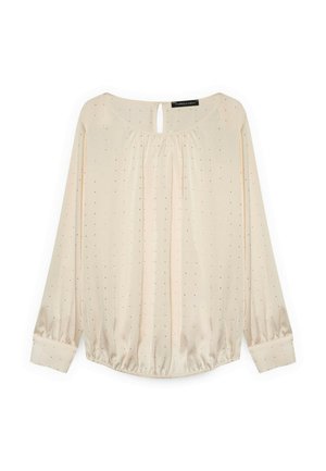 Blusa de manga larga color beige claro con cuello fruncido, detalle de ojal, puños elásticos y pequeños lunares negros en toda su superficie.