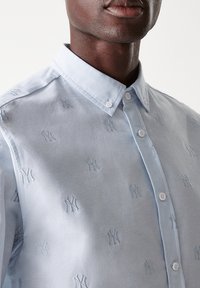 Camicia azzurro chiaro con bottone e piccoli loghi NY ricamati, dotata di colletto classico e superficie liscia.