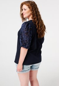 Navyblauwe shirt met bloemengeborduurde doorschijnende mouwen en een relaxte pasvorm. Gecombineerd met lichte denim shorts.