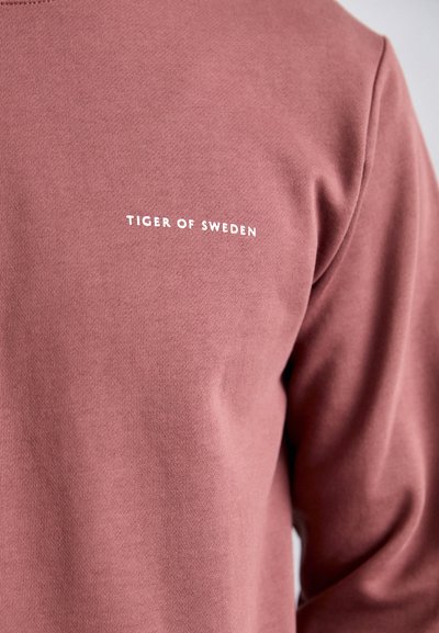Bordó kapucnis pulóver puha pamutból, lekerekített nyakkivágással. Fehér "TIGER OF SWEDEN" felirat található a bal mellkas területén. Sima textúra.