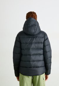 Svart boblejakke med hette, med et quiltet design, glatt tekstur og en tettsittende silhuett. Brukt over grønne cargo-bukser.