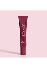 Tubetto bordeaux di Teaology Tea Gloss con testo bianco. Texture liscia, design affusolato e tappo a vite. Ambientato su uno sfondo rosa chiaro.