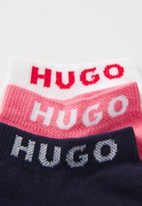 Drei Paar Socken in Weiß, Pink und Marineblau. Jede Socke hat "HUGO" in kontrastierenden Farben an der Spitze eingewebt. Weicher, strukturierter Stoff.
