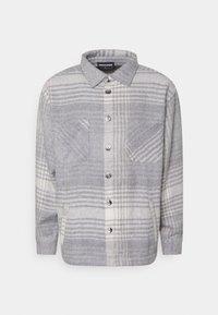 Camicia a quadri grigia e crema in un morbido tessuto spazzolato. Presenta una chiusura con bottoni, due tasche sul petto e un colletto classico.