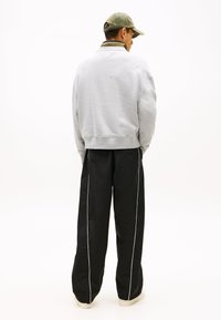 Γκρι φούτερ με κομμένο σχέδιο, συνδυασμένο με μαύρο παντελόνι με φαρδιά μπατζάκια και αντίθετες λευκές πλευρικές ρίγες, και πράσινο καπέλο.