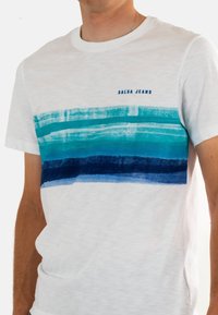 Camiseta blanca de manga corta con un diseño de rayas horizontales en turquesa y azul marino, con el texto "SALSA JEANS" en azul.