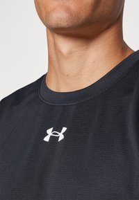 Fekete sportpóló kerek nyakkivágással, texturált anyagból, fehér Under Armour logóval a mellkason.