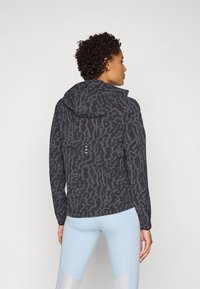 Black and gray patterned jacket with a hood, featuring a soft texture, rear vent, and reflective details, paired with light blue leggings.