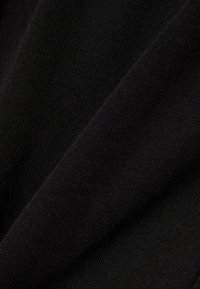 Close-up van zwarte stof met zichtbare breistructuur en diagonale plooien die schaduwcontrasten creëren.