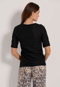 Zwarte textuur top met korte mouwen en een golvend patroon, gecombineerd met gestreepte broek met een geometrisch ontwerp in meerdere kleuren.