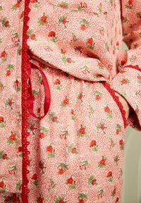 Set de pijamale florale roșii cu un fundal texturat deschis, având un detaliu din dantelă și un nod din satin. Croit cu o tăietură largă și confortabilă.