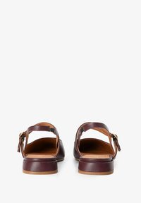 Sandales en cuir marron avec un petit talon, dos ouvert et sangle réglable. Texture lisse avec une doublure intérieure beige et un détail de quincaillerie minimal.