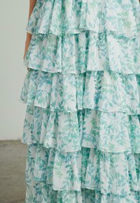 Vestido arrugado de tela azul claro con un patrón de acuarela verde con hojas; múltiples capas crean una apariencia texturizada y estratificada.