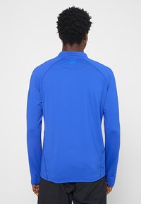 Koszulka sportowa z długim rękawem w jaskrawym niebieskim kolorze, z teksturowanym materiałem, bezszwowym wykończeniem ramion i subtelnym detalem logo na plecach.