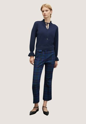 Navy blouse with ruffled collar and cuffs, paired with plaid trousers in blue and green shades, finished with black, pointed flats.