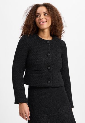 Giacca in tweed nera con scollo rotondo, maniche lunghe e tasche frontali. Presenta cinque bottoni neri e un tessuto testurizzato con un sottile luccichio.