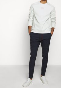 Light gray sweatshirt with ribbed cuffs and a small logo. Dark navy joggers with a red drawstring and tapered legs. White sneakers.