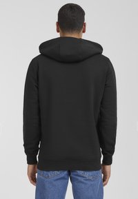Black hooded sweatshirt with a kangaroo pocket, ribbed cuffs, and hem. Material appears soft and slightly textured. Worn with light blue jeans.