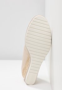 Chaussure beige avec une tige en tissu texturé, une semelle en caoutchouc blanche comportant des rainures horizontales, et un design à bout arrondi.