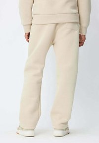 Pantalons de survêtement beige clair en tissu doux, dotés d'une coupe décontractée, d'une taille élastique et d'une poche latérale à l'arrière.