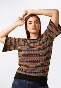 Gestickter Pullover mit einem Zickzackmuster in Grün, Rot und Schwarz; kurze Ärmel mit gewellten Kanten; schwarzer gerippter Saum.