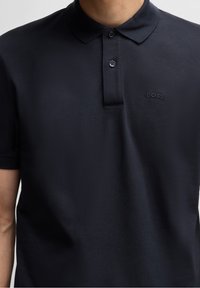 Tmavě modré polo tričko z texturované látky, s klasickým límcem a trojím knoflíkovým zapínáním s malým vyšitým logem "BOSS".