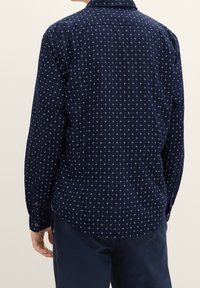 Marinblå långärmad skjorta med ett vitt geometriskt mönster av små kors, knappmanschetter och standardkrage, tillverkad av lättviktsmaterial.