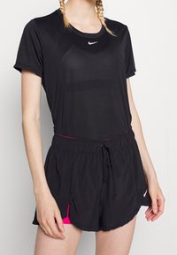 Camiseta atlética negra con cuello redondo y mangas cortas, acompañada de pantalones cortos negros con un forro interior rosa y aberturas laterales.