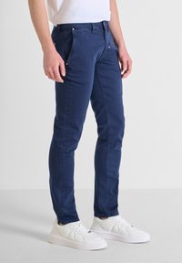 Námořnické modré pružné džíny s úzkým střihem, se zapínáním na zip, předními kapsami a stříbrnými doplňky, spárované s bílými teniskami.