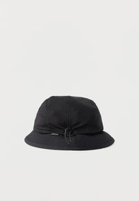 Μαύρο καπέλο τύπου κουβά με ρυθμιζόμενο κορδόνι και μικρή υφασμάτινη ετικέτα μάρκας στη γείσο, υφή ύφασμα στην επάνω περιοχή.