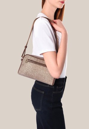 Borsa a tracolla marrone e beige con texture, dotata di tasca frontale con zip, design slim e tracolla regolabile, tenuta da una persona che indossa una camicia bianca.