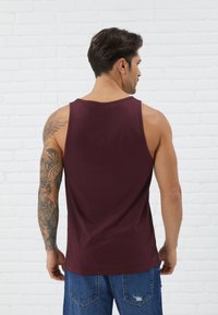 Burgundy tank top with a classic cut, made from soft fabric. Shows back view, featuring smooth texture and rounded neckline.