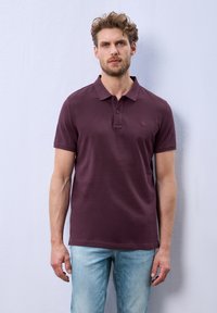 Polo en bordeaux avec manches courtes, col classique et trois boutons. Fabriqué dans un tissu lisse, avec un logo discret sur la poitrine.