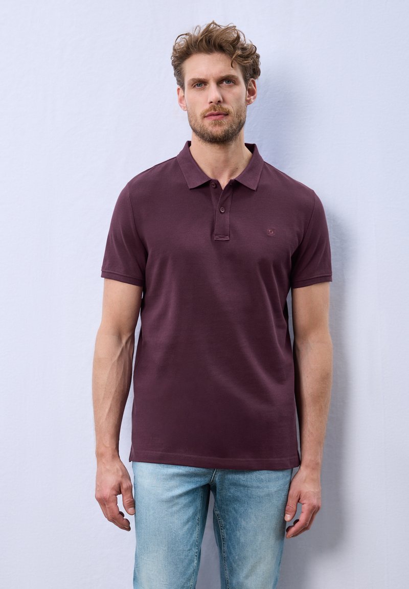 Polo en bordeaux avec manches courtes, col classique et trois boutons. Fabriqué dans un tissu lisse, avec un logo discret sur la poitrine.