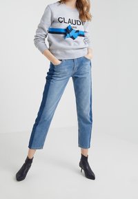 Szara bluza z napisem "CLAUDIA PARIS", niebieskie paseczki, do tego jasnoniebieskie dżinsy o prostym kroju sięgające do kostek.