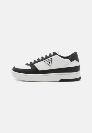 Zapatilla blanca y negra que presenta materiales de cuero y sintéticos, puntera redonda, suela gruesa y logotipo triangular en el lado exterior.