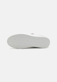 Fehér sneaker talp, texturált grip mintával, lekerekített éllel és logó részlettel. Az anyag guminak tűnik, sima felülettel.