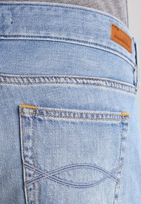 Tasca posteriore di jeans in denim azzurro con cuciture decorative e un'etichetta in pelle marrone di Abercrombie & Fitch sulla cintura.