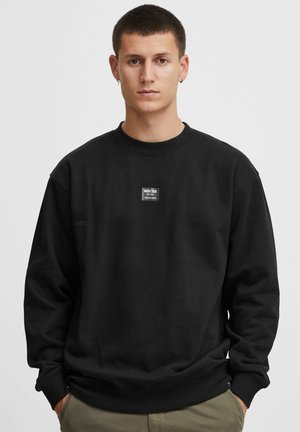 Sudadera negra con cuello redondo, puños y dobladillo de canalé. Presenta un pequeño parche rectangular con el logotipo en el pecho. Material de algodón.