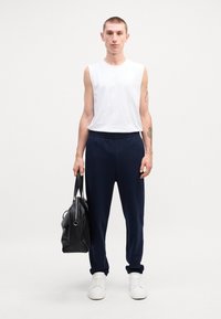 Camiseta sin mangas blanca, pantalones elásticos de cintura azul marino y zapatillas blancas. Una bolsa negra se sostiene en la mano derecha. Diseño sencillo y minimalista.