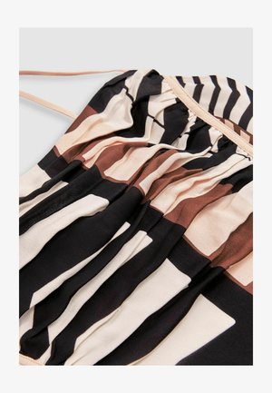 Pogled od blizu na tkanino z črnimi, bež in rjavimi geometrijskimi črtami in naborki, ki ima tanek bež trak na svetlem ozadju.