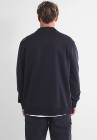 Sweatshirt bleu marine à manches longues, col rond et coupe décontractée. Caractérisé par une texture lisse et des bords côtelés aux manches et en bas.