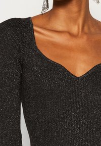 Maglia nera a maglia con scollo a V profondo e maniche lunghe, realizzata in un tessuto testurizzato con accenti di leggera lucentezza.