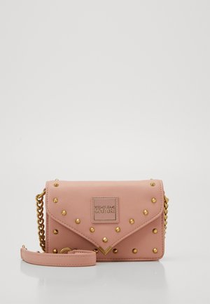 Sac bandoulière rectangulaire rose avec clous dorés, bandoulière en chaîne et patch central portant l'inscription "Versace Jeans Couture" sur un fond épuré.
